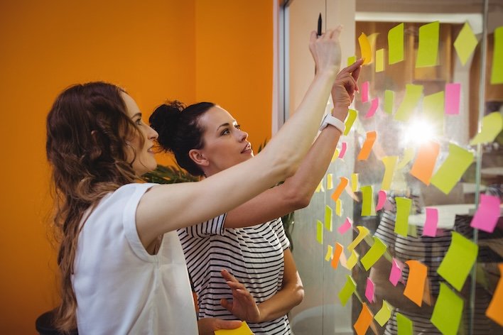 Postit yapıştırılı bir alanın önünde drup postitleri güncelleyen bir takım görseli.
